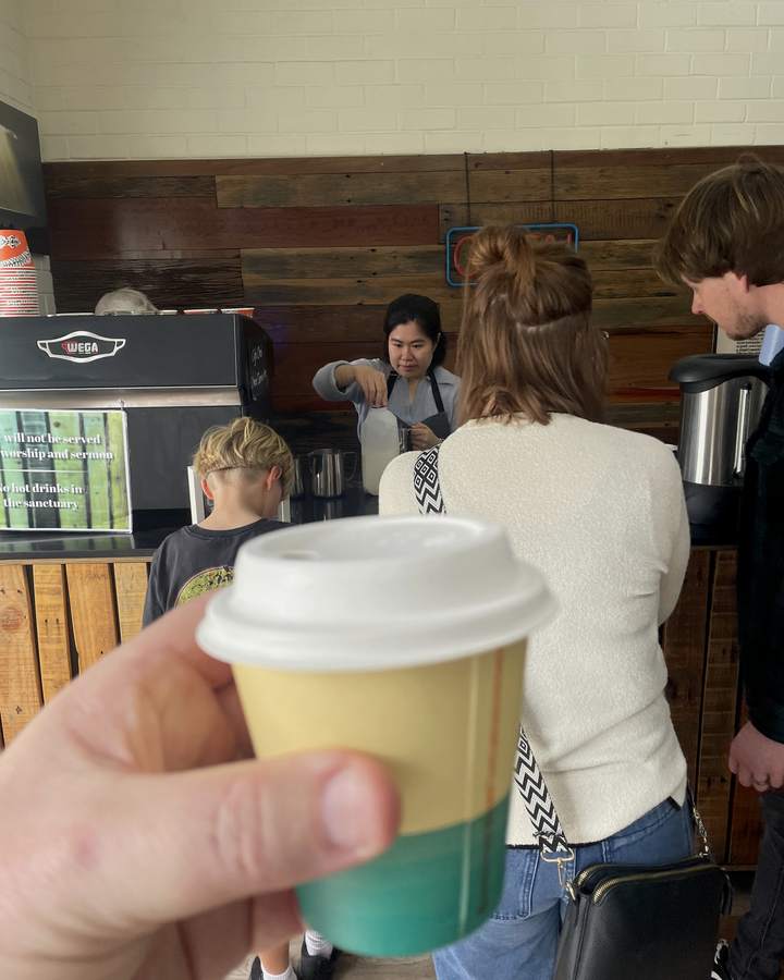 A coffee in hand in the Calvary cafe, with people catching up on a Sunday